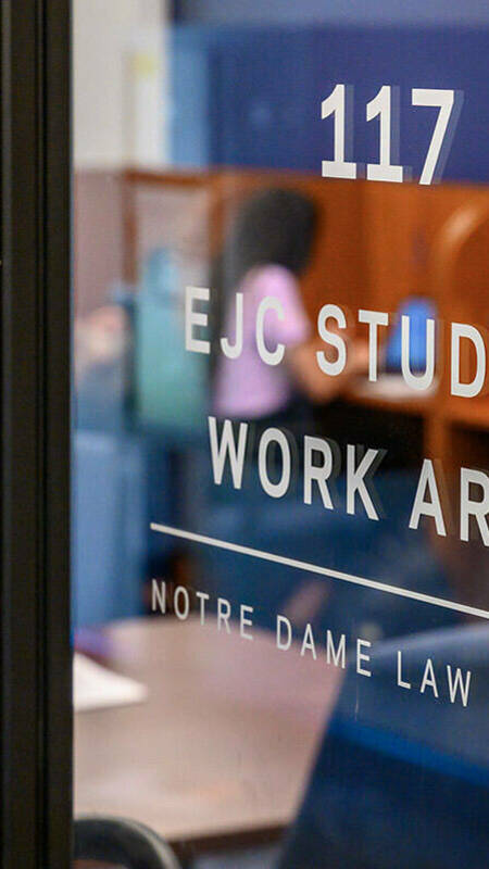 A glass door in the Notre Dame Law School leads to room 117, the EJC Student Work Area