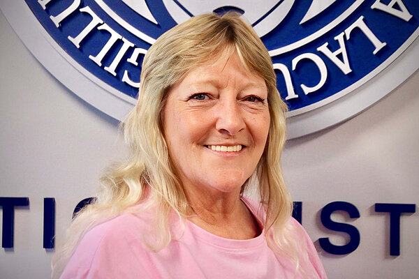 Blonde woman in a pink shirt smiling in front of a raised blue and white sign at Notre Dame.