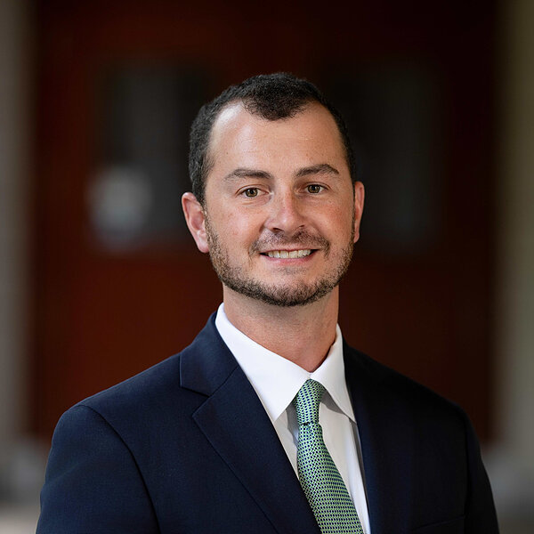 Man in a dark suit, white shirt, and green patterned tie smiles gently. (Kevin Murphy)